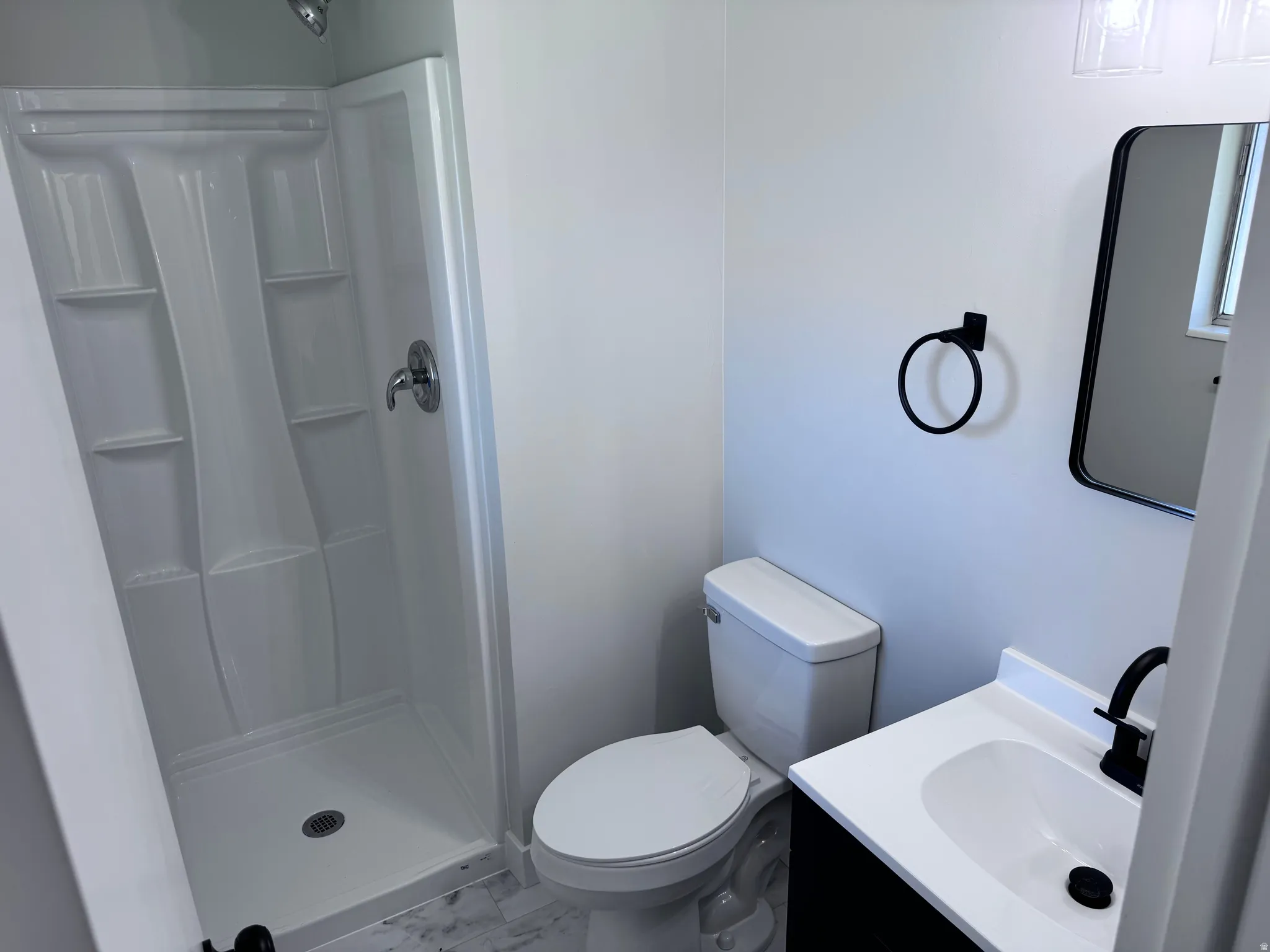 Shower with built-in shelving, white vanity with integrated sink, dark cabinetry, and matte black fixtures