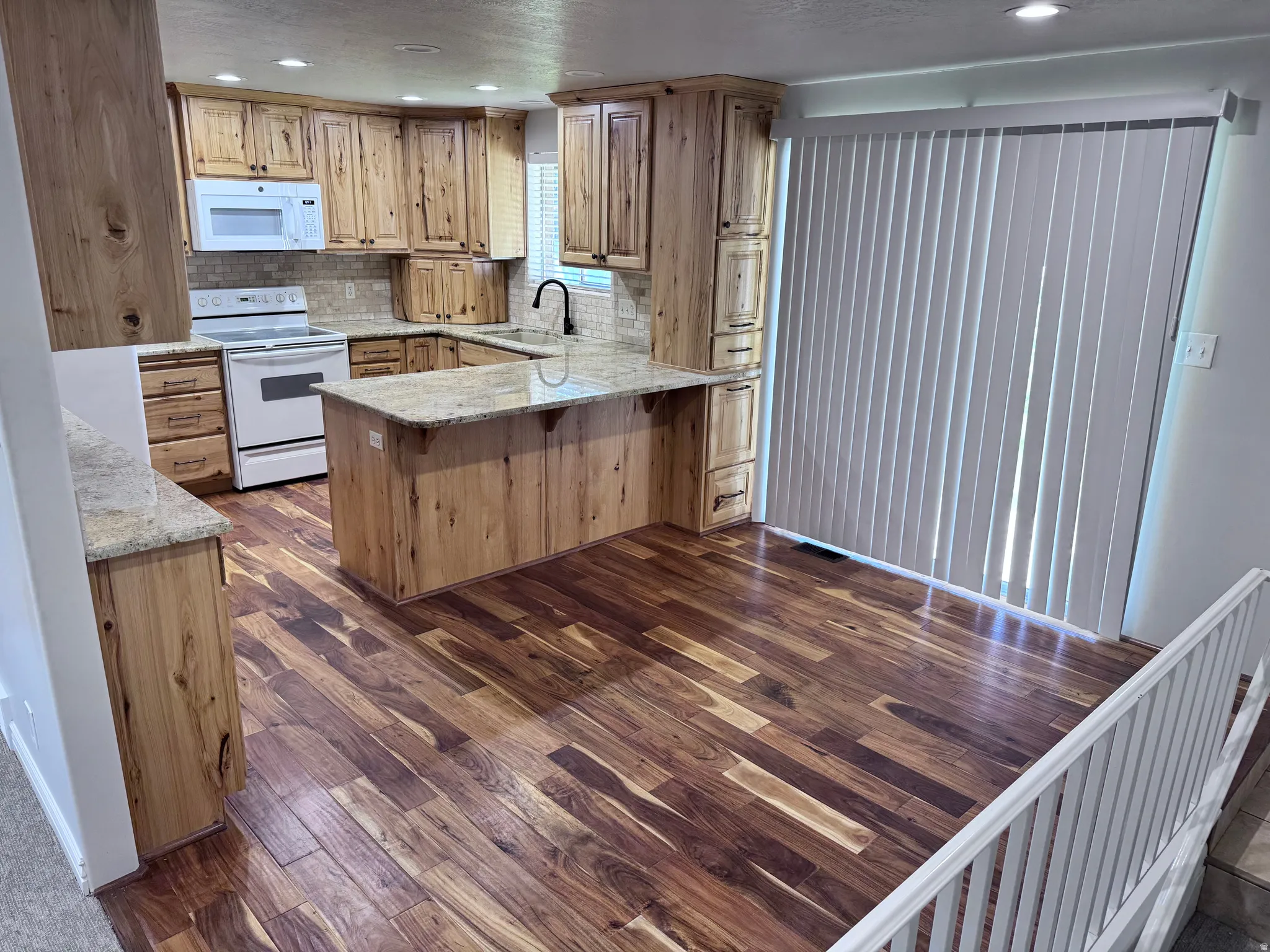Kitchen featuring extensive wood cabinetry, granite countertops, a central island, wood-finish flooring, and white appliances