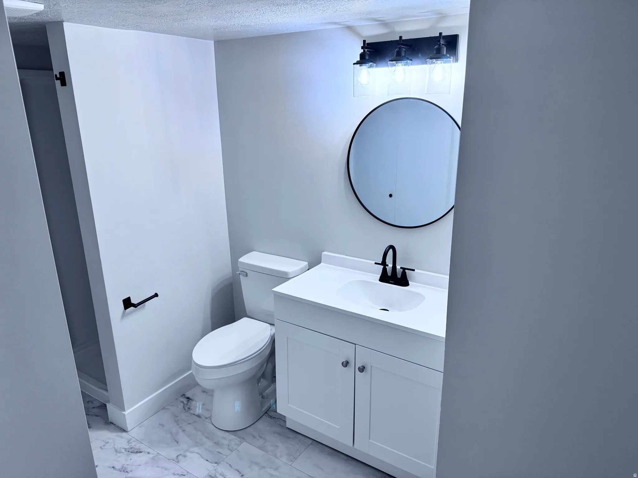 White shaker-style vanity with chrome pulls, black matte faucet, and round mirror