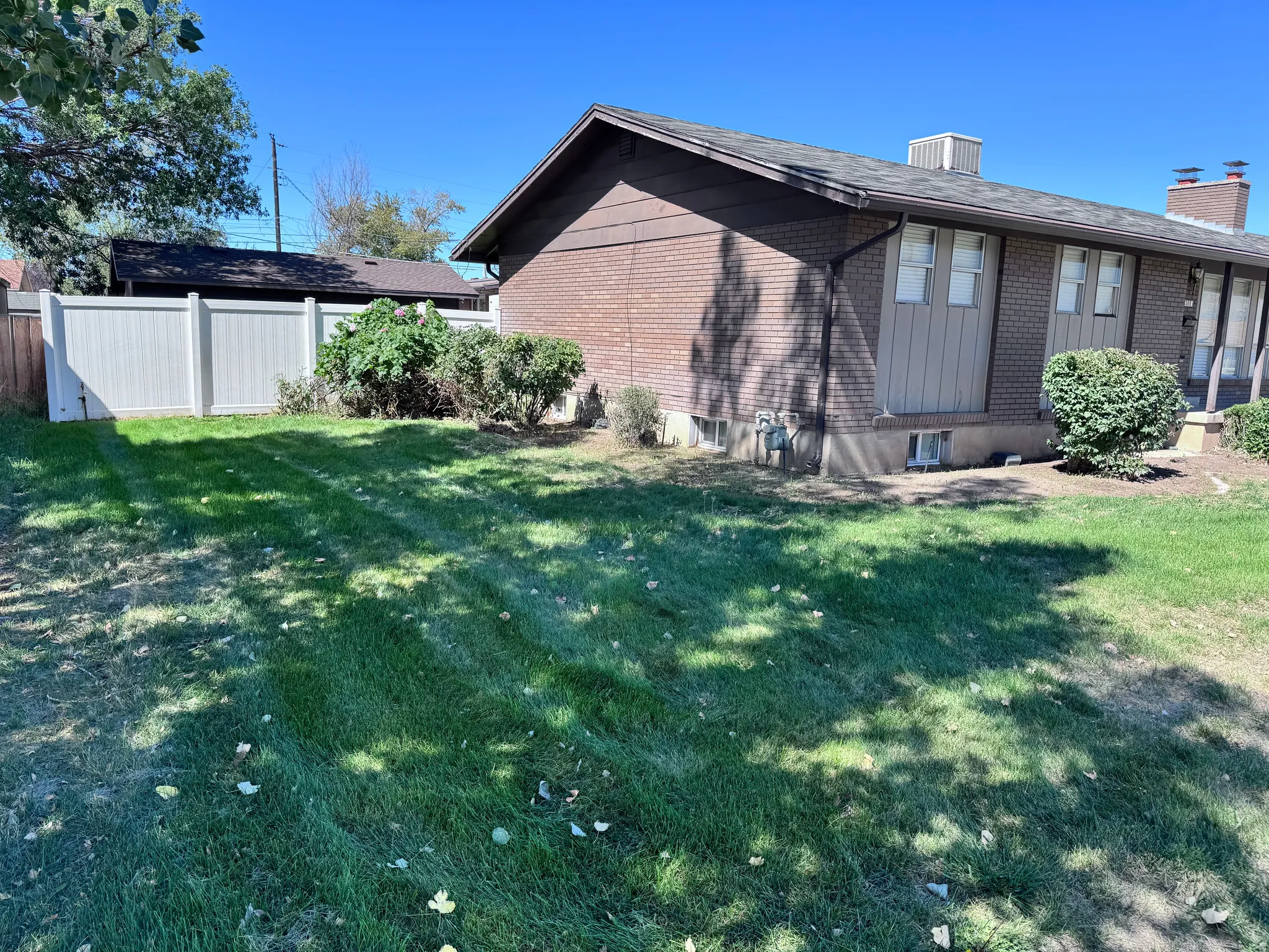 Brick exterior with vertical siding accents, a shingle roof, established landscaping, and a fenced perimeter