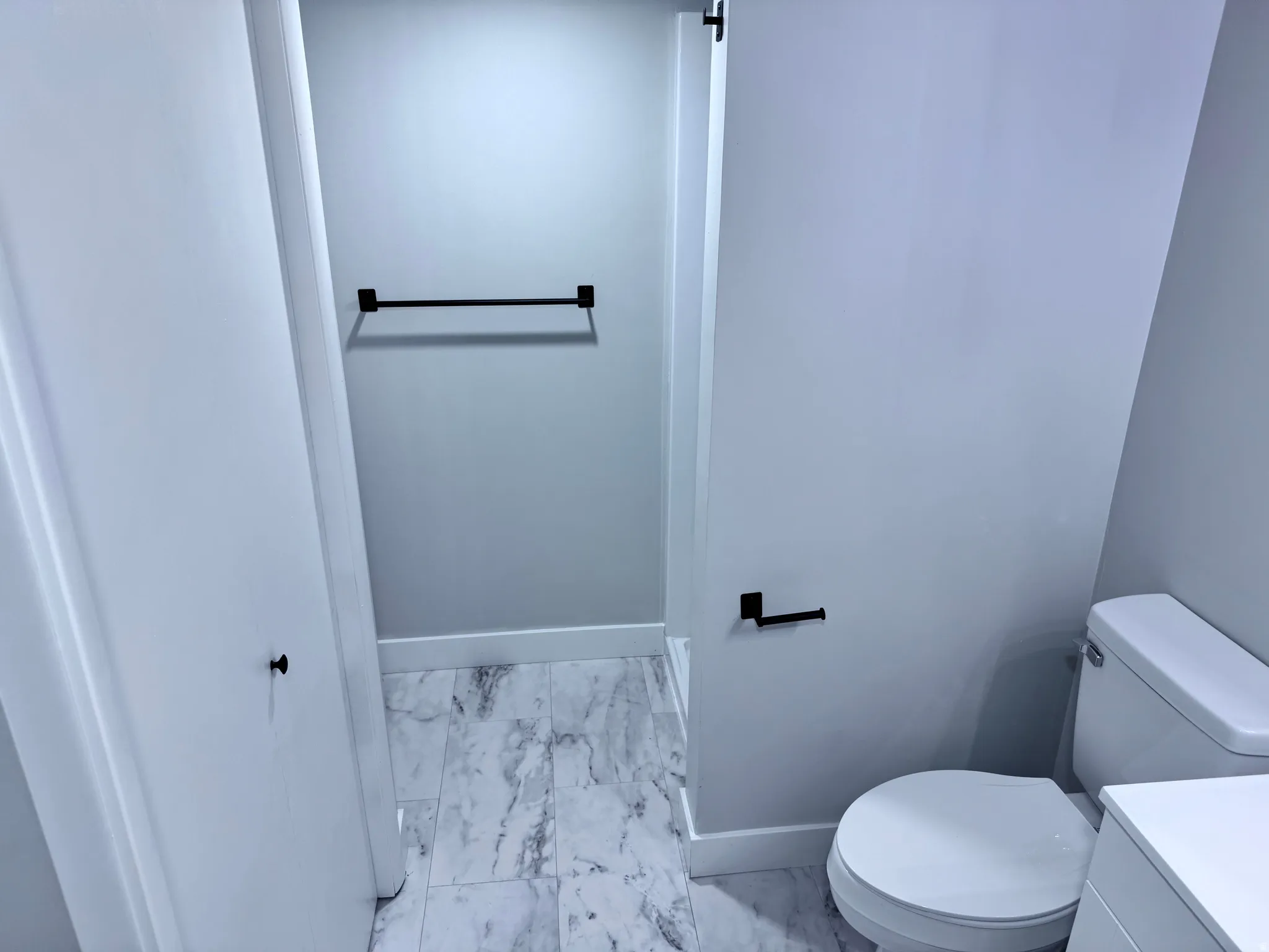 White marble-patterned flooring, black hardware accents, and a white toilet
