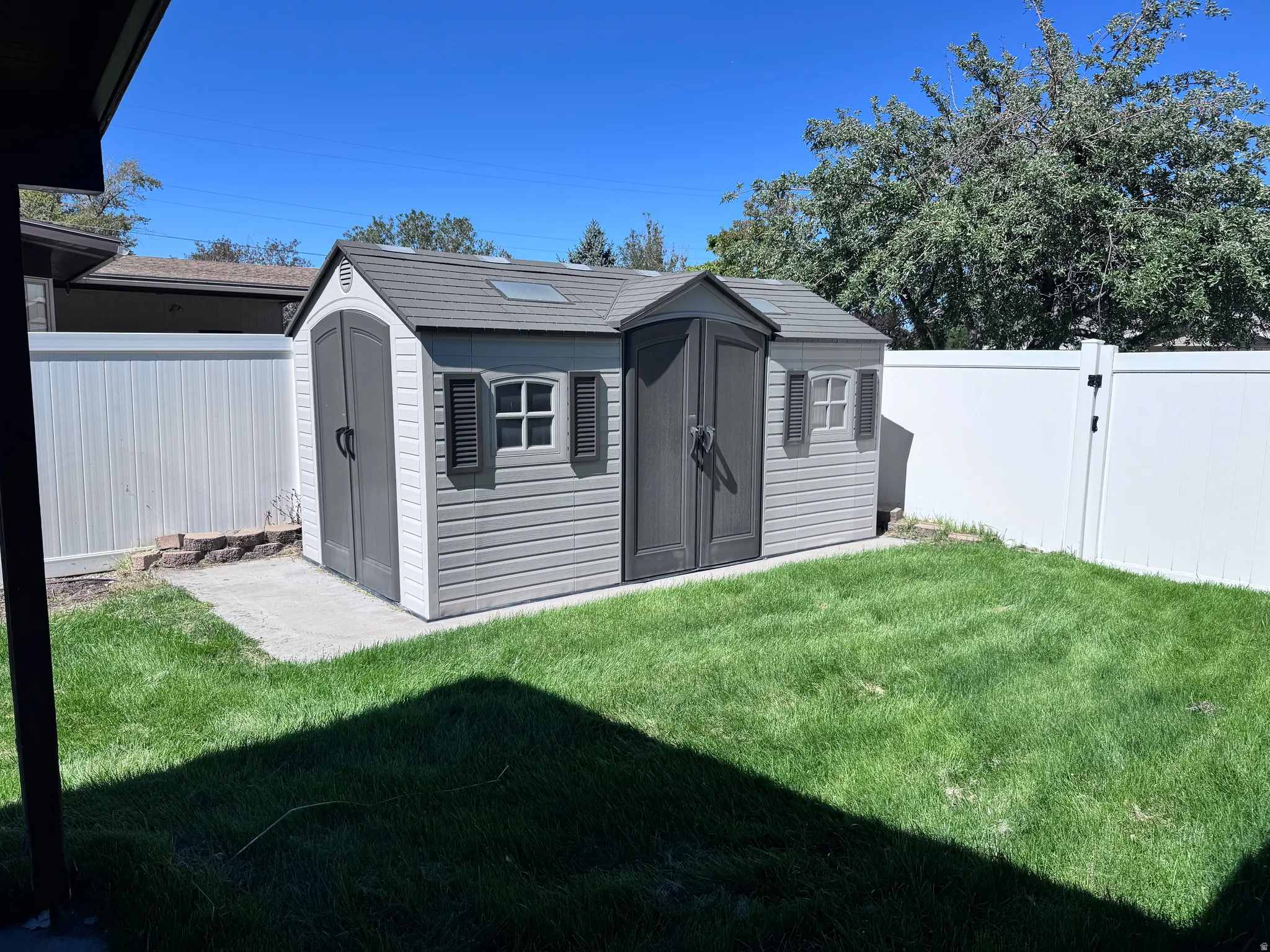 Private backyard featuring a storage shed with dual doors and windows, a concrete pad, a vinyl fence, and a grassy area