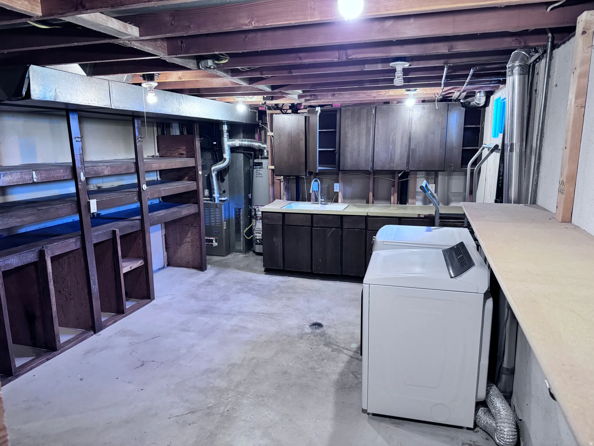 Exposed wood beam ceiling, concrete flooring, built-in shelving, dark wood-finish cabinetry, and a utility sink