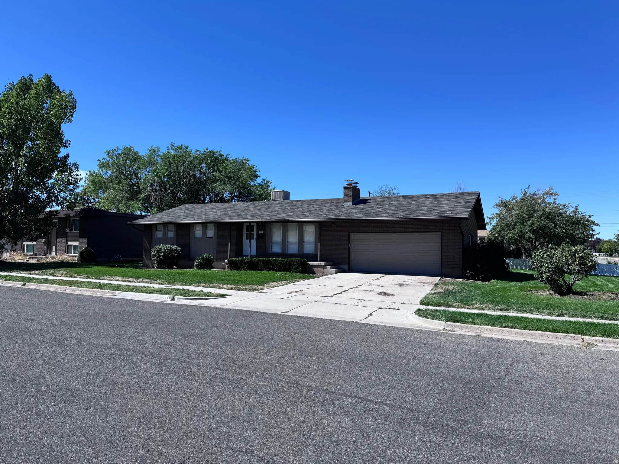 Ranch-style residence featuring a prominent front lawn, mature trees, and an attached garage with a paved driveway