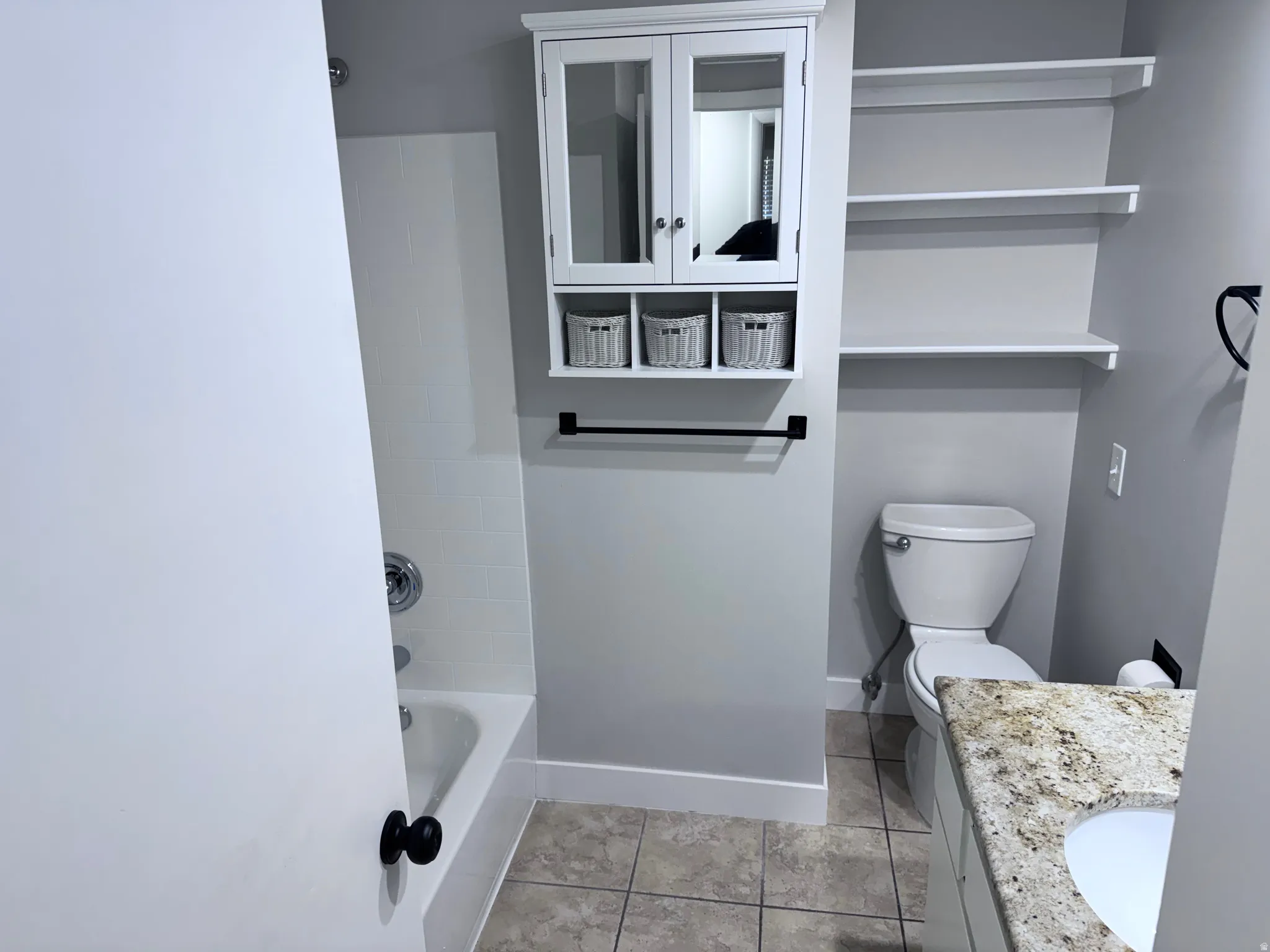 Bathroom featuring a white bathtub with tile surround, built-in shelving, a wall-mounted medicine cabinet, and a vanity with a light-colored countertop and integrated sink