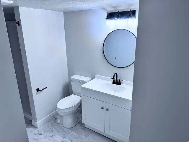 White shaker-style vanity with chrome pulls, black matte faucet, and round mirror