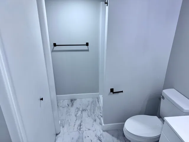 White marble-patterned flooring, black hardware accents, and a white toilet