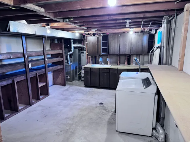 Exposed wood beam ceiling, concrete flooring, built-in shelving, dark wood-finish cabinetry, and a utility sink