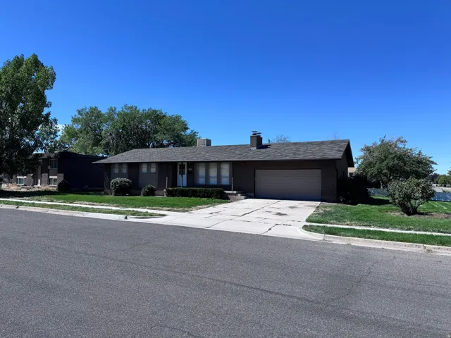 Ranch-style residence featuring a prominent front lawn, mature trees, and an attached garage with a paved driveway