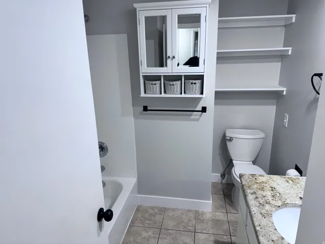 Bathroom featuring a white bathtub with tile surround, built-in shelving, a wall-mounted medicine cabinet, and a vanity with a light-colored countertop and integrated sink