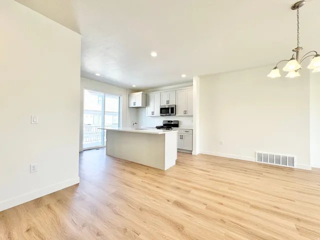 Wood-finish flooring throughout, recessed lighting, modern white cabinetry, stainless steel appliances, and a kitchen island with a white countertop