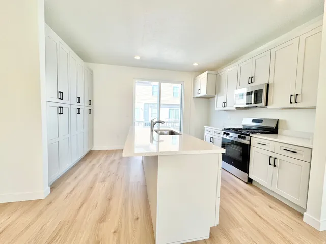 Modern kitchen with light wood-finish flooring, white shaker cabinetry, stainless steel appliances, a center island with sink, and solid surface countertops