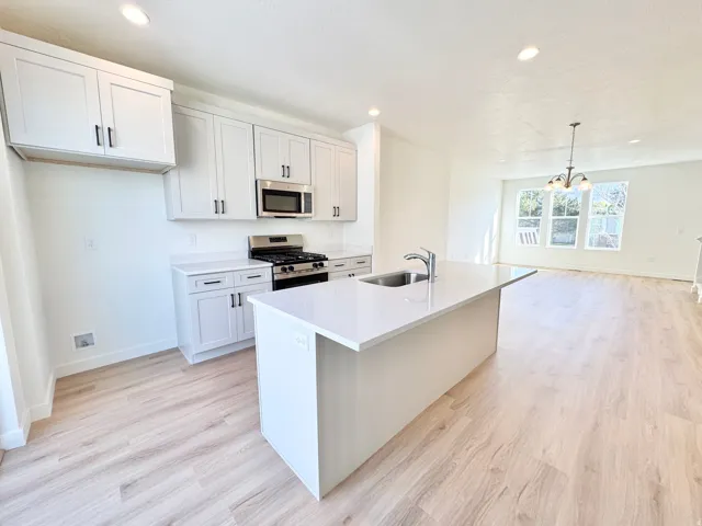 Kitchen featuring a center island with an integrated sink, stainless steel appliances, white cabinetry with dark hardware, and light wood-finish flooring