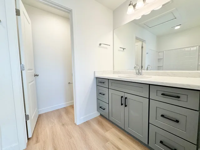 Vanity with a single basin sink, light-toned countertop, and grey cabinetry with black hardware