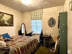 Carpeted room with a single window and ceiling-mounted light fixture. Bedroom located in the house.