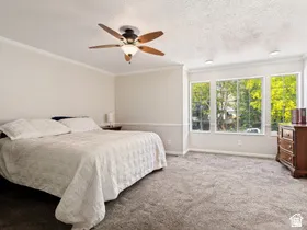 Wall-to-wall carpeting, multiple windows with exterior scenery, crown molding, and a ceiling fan with integrated lighting