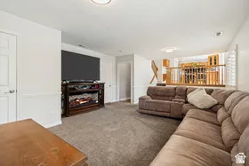 Carpeted living area featuring a built-in electric fireplace and wood-finish mantel, with a partial view of a staircase and upper-level railing