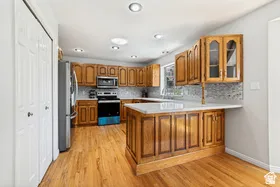 Kitchen featuring wood-finish cabinetry, stainless steel appliances, light-toned countertops, and mosaic tile backsplash