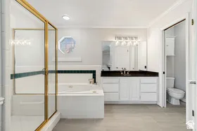 Recessed lighting, large vanity with dual sinks, built-in bathtub with tile surround, separate shower with glass enclosure, and tiled flooring