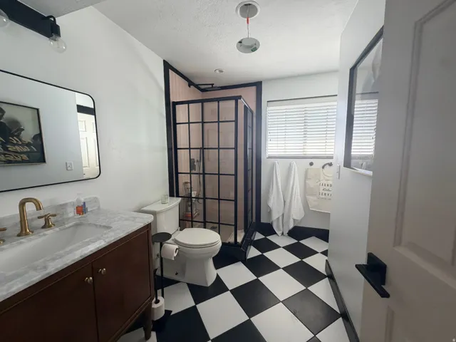 Bathroom featuring a dark wood-finish vanity with a light-toned countertop, a gold-toned faucet, a black-framed mirror, and a black and white checkerboard floor