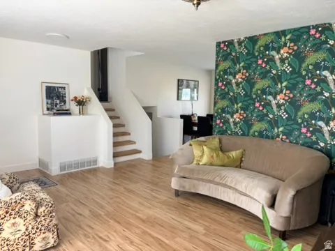 Wood-finish flooring throughout, staircase with wood treads, accent wall featuring botanical wallpaper, and white painted walls