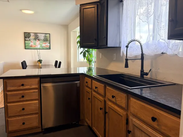 Black countertops, stainless steel dishwasher, black sink, black faucet, and wood-finish cabinetry
