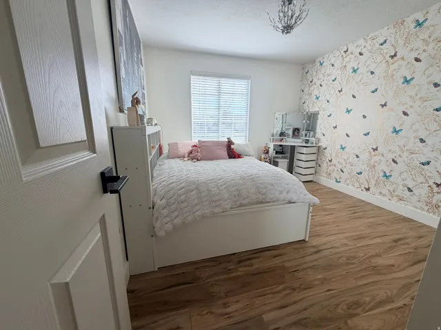 Wood-finish flooring, white trim, recessed window with blinds, and an overhead chandelier