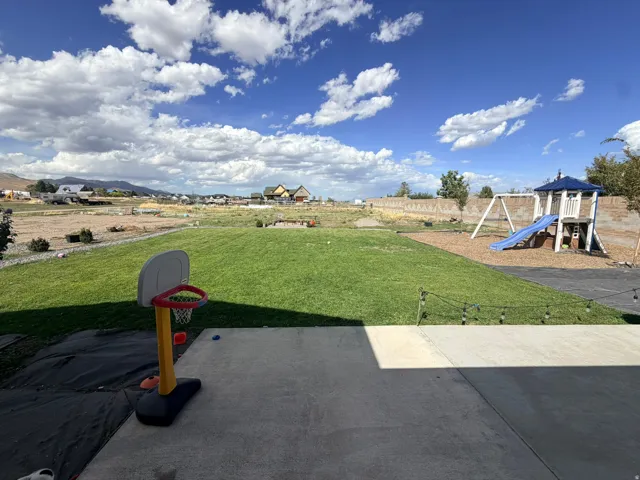 Expansive backyard featuring a large concrete patio, manicured lawn, and a dedicated play area with wood chip ground cover