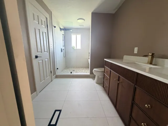 Spacious bathroom featuring a double vanity with ample storage, a walk-in shower with tile surround and pebble flooring, and large format floor tiling