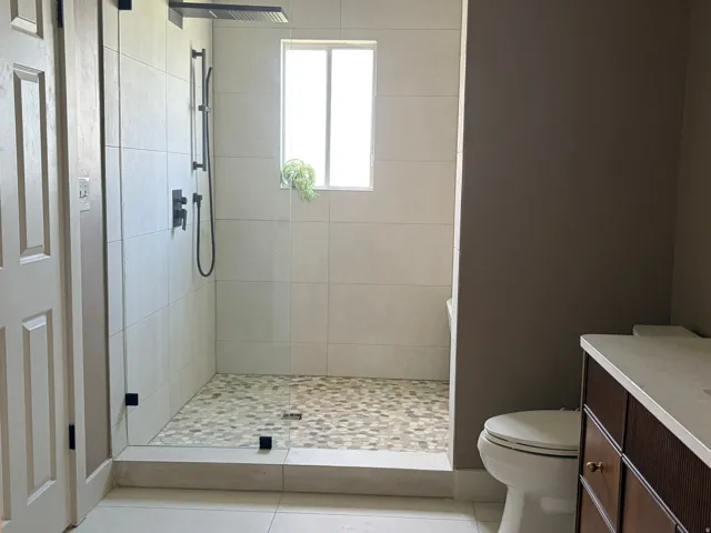 Glass-enclosed shower with a rainfall showerhead, handheld sprayer, and mosaic pebble tile flooring
