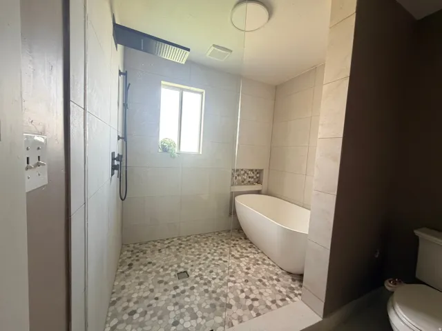 Walk-in shower with pebble tile flooring and a matte black rain shower head, alongside a freestanding soaking tub with a tiled niche
