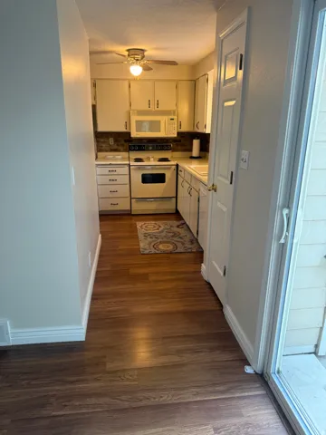 Kitchen featuring wood-finish flooring, white cabinetry, a built-in microwave, and a ceiling fan