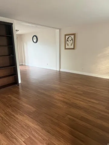 Wood-finish flooring throughout, bright white wall paint, and a built-in dark wood shelving unit