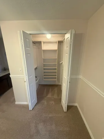 Master bedroom walk-in closet with built-in shelving, hanging rods, and carpet flooring