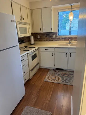 Kitchen featuring wood-finish flooring, white cabinetry, a brick-style backsplash, and a window above the sink
