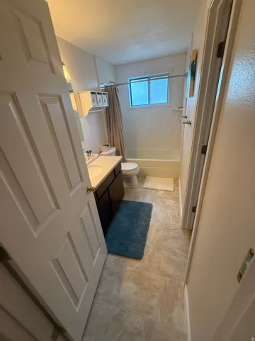 Windowed bathroom featuring a built-in tub with shower, single vanity, and tiled flooring