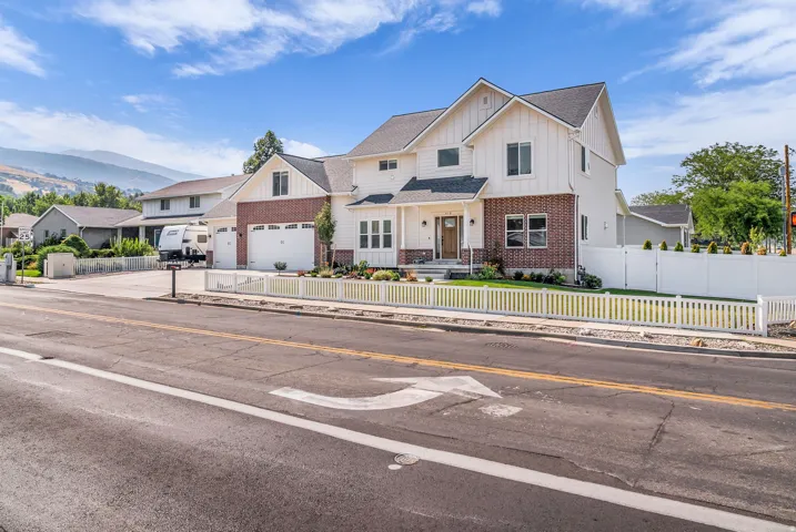 Two-story residence featuring white siding and brick accents, a three-car garage, a covered front porch, and a white picket fence