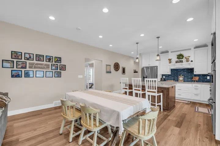 Recessed lighting illumination, wood-finish flooring, white cabinetry, kitchen island with seating, and a blue tile backsplash