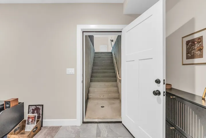 ADU Entry from garage stairs. Welcoming foyer with white panel door, polished wood-finish flooring, and direct access to basement stairs