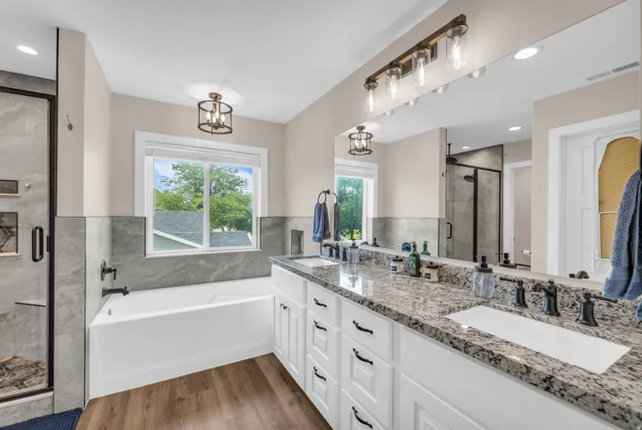 Master Bath Double vanity with granite countertop, wood-finish flooring, a soaking tub, and a glass-enclosed shower