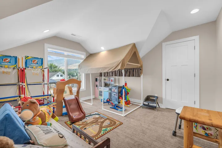 Carpeted room with sloped ceilings, recessed lighting, a large window, and a paneled white door