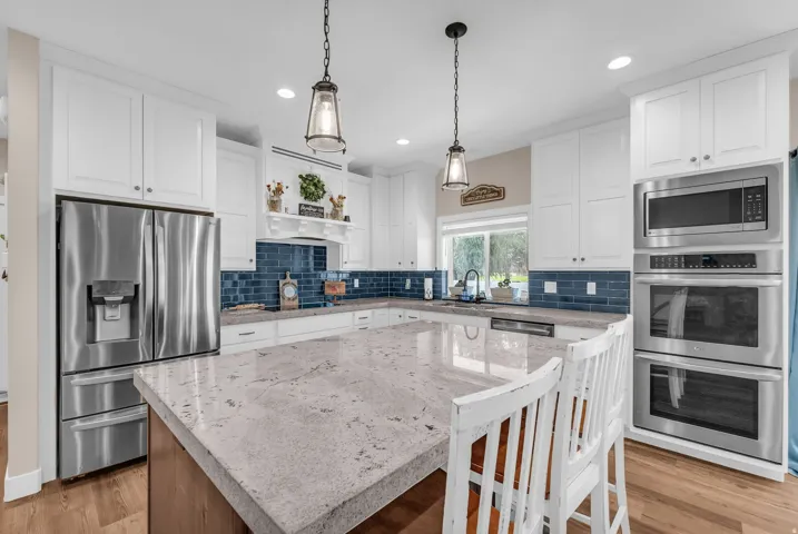 Kitchen featuring white cabinetry, stainless steel appliances, a large center island with a light-toned countertop, and a blue tile backsplash