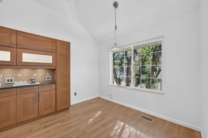 Vaulted ceiling, wood-finish flooring, built-in cabinetry with glass-front accents, and a large window letting in natural light.