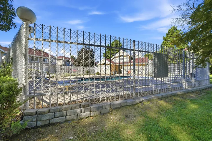 Fenced outdoor pool area featuring a chain-link fence, brick retaining wall, and surrounding green space