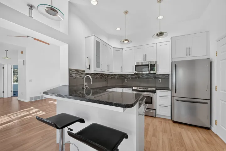 Kitchen featuring white cabinetry, granite countertops, stainless steel appliances, and a mosaic tile backsplash.  All appliances stay.