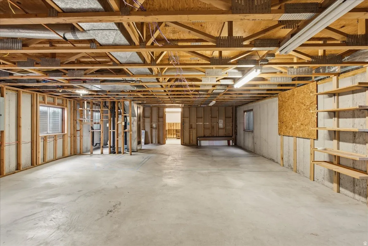 Unfinished basement featuring exposed wood joists, concrete flooring, and built-in shelving