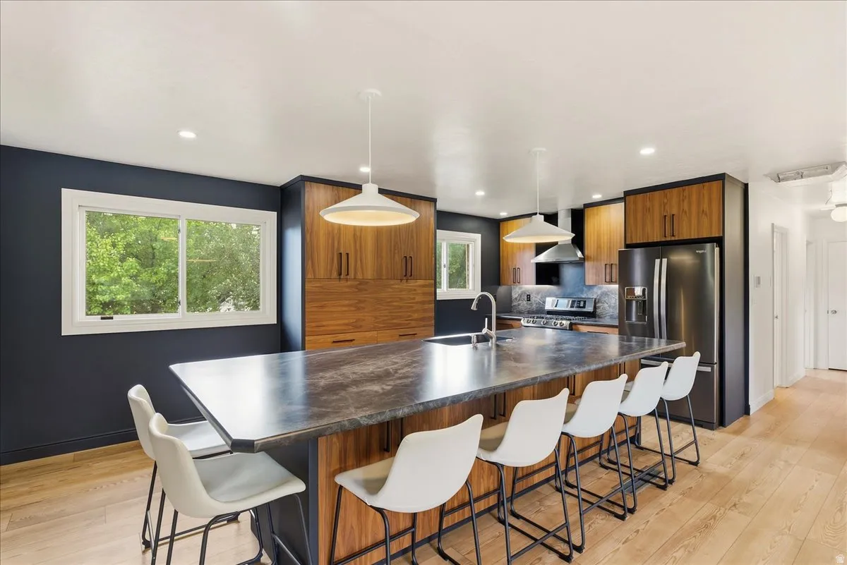 Expansive kitchen island with seating, wood-finish cabinetry, stainless steel appliances, and wood-finish flooring