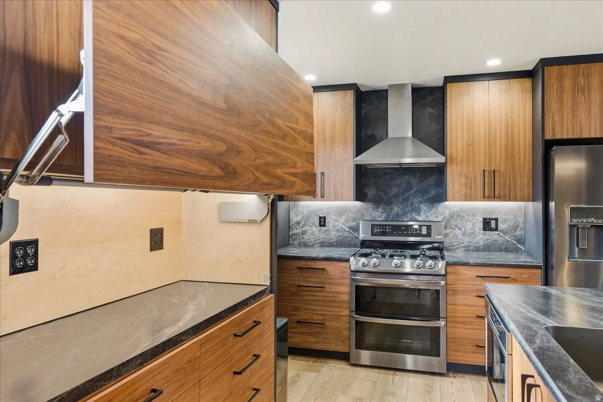 Wood-finish cabinetry, stone slab countertops, stainless steel appliances, under-cabinet lighting, and recessed ceiling lighting
