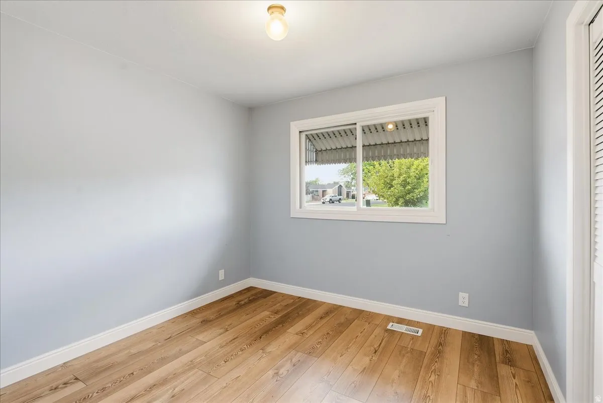 Wood-finish flooring, light blue wall paint, white trim, sliding window, and a built-in closet with louvered doors