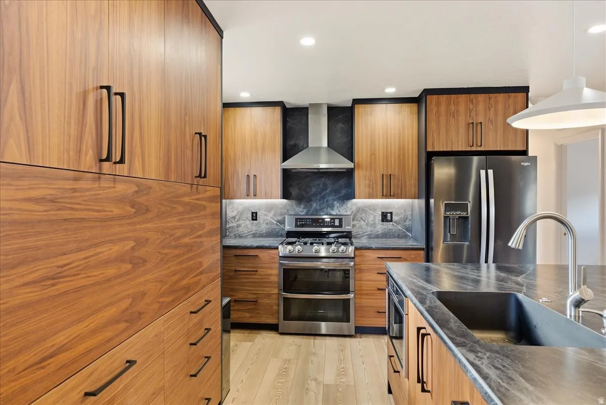Wood-finish cabinetry, dark stone countertops, stainless steel appliances, recessed lighting, and wood-finish flooring